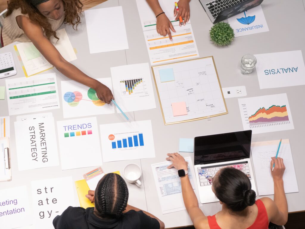 a group of people working at a large table covered in papers with graphs, representing the importance of ISO documentation services