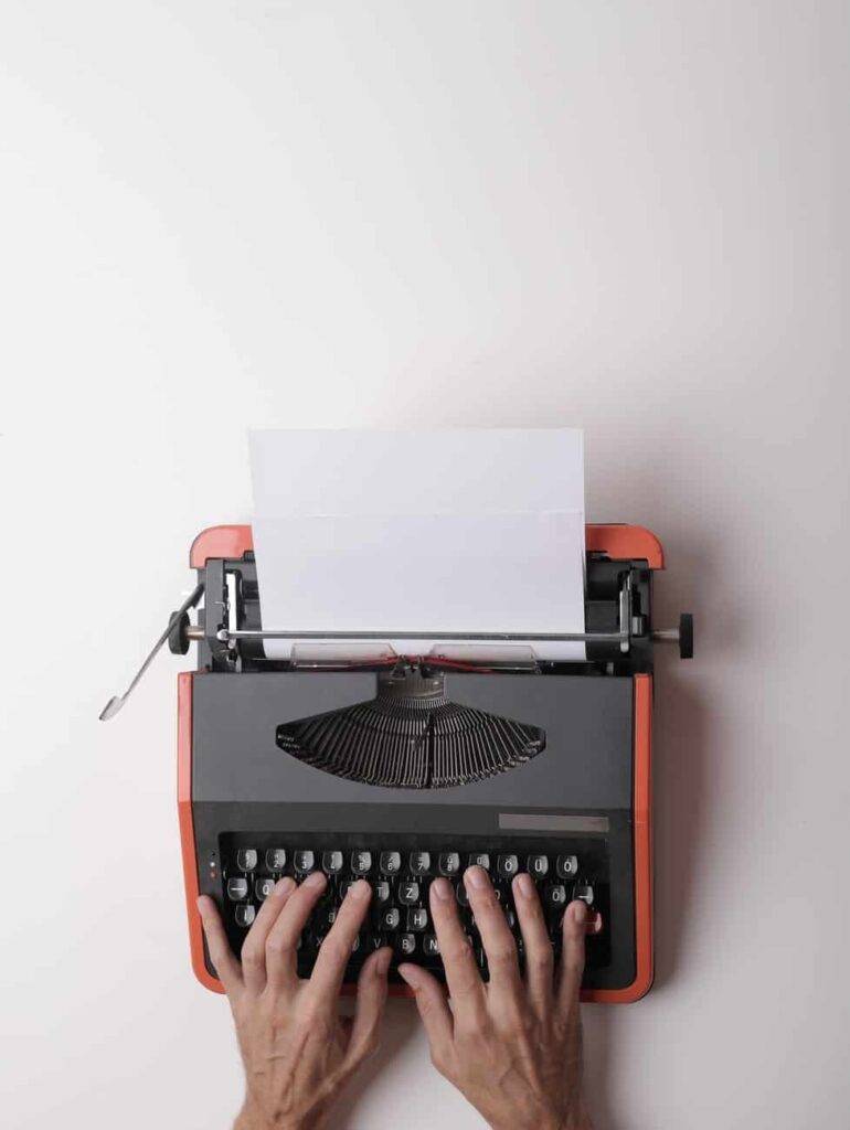 A set of hands typing into a red and black typewriter