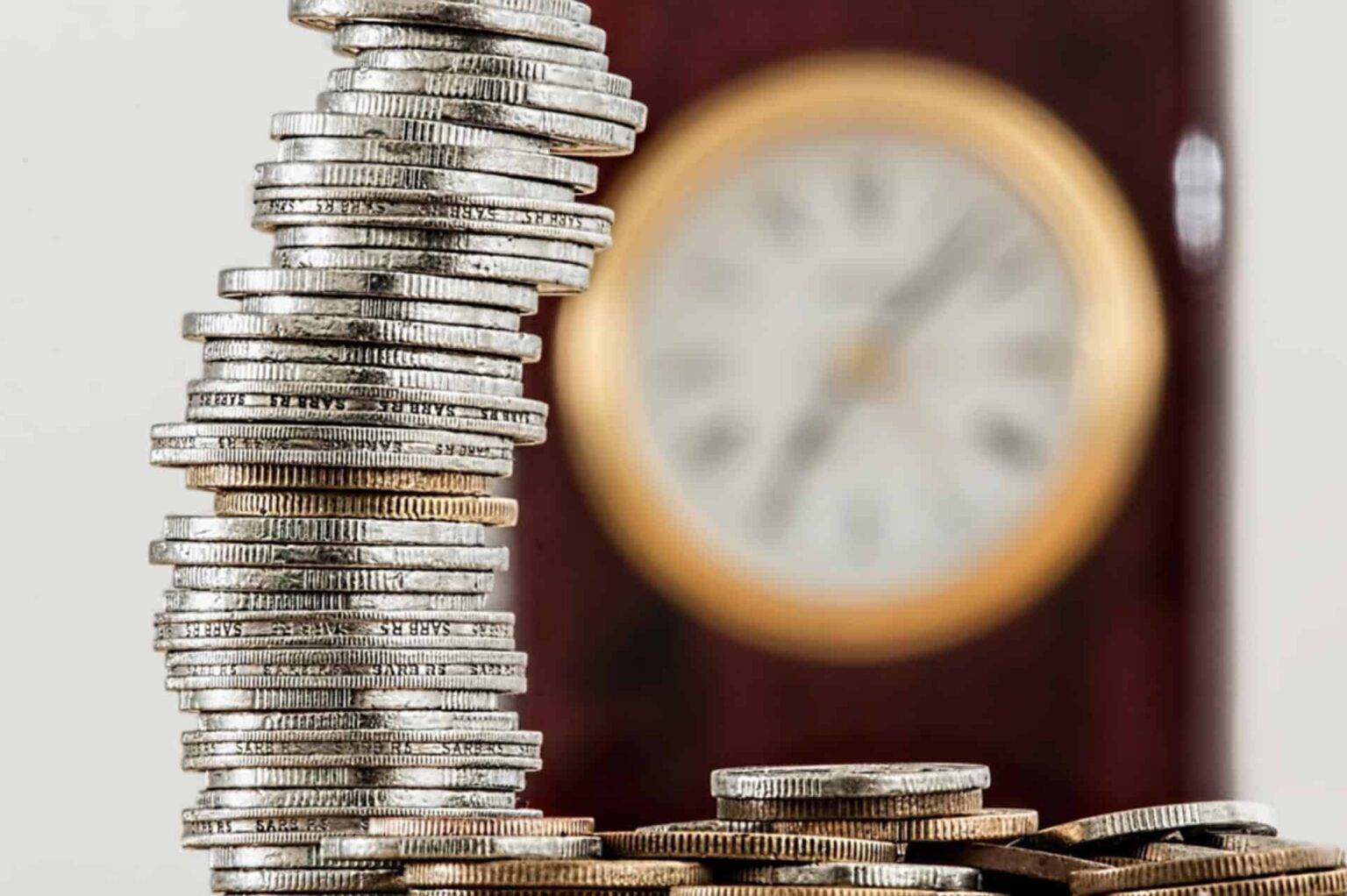 Silver coins stacked and a clock in the background with a bokeh effect