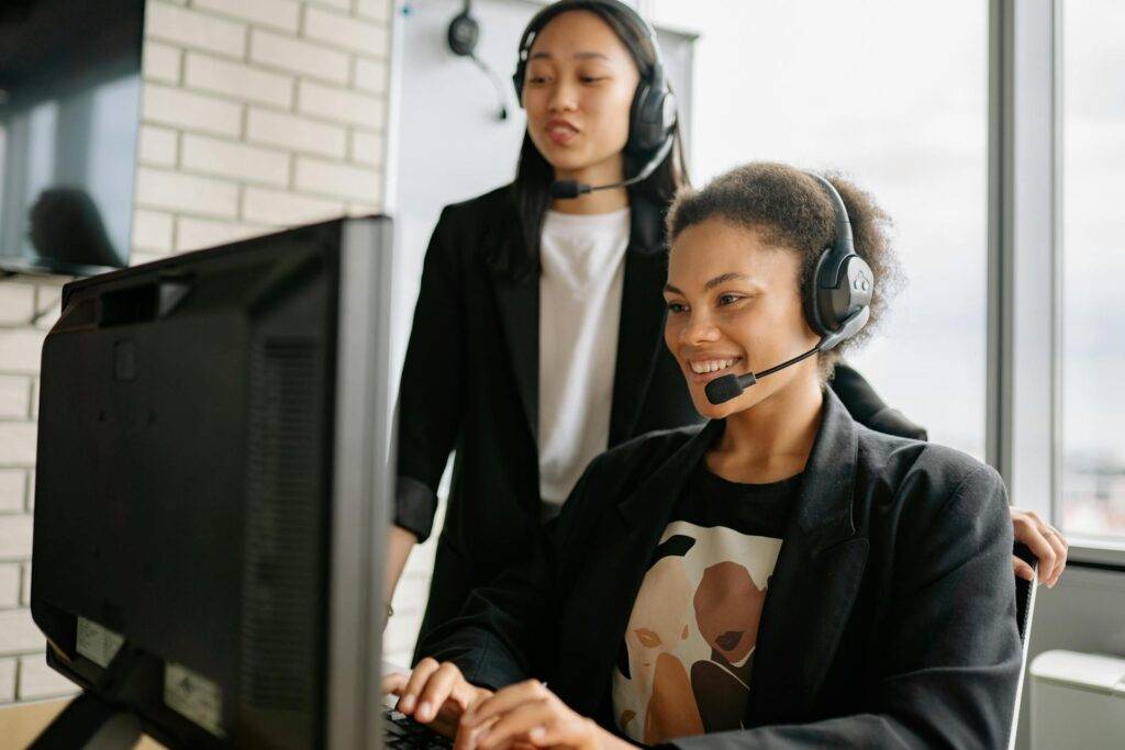 two People Smiling While Working Together on a Computer, Representing the Benefits Business Operations Manuals Can Have for Efficiency and Team Morale