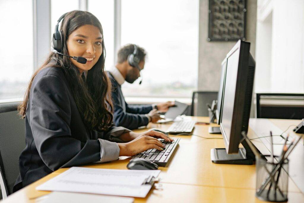 an Employee Wearing a Headset, Smiling While Sitting at a Desk, Representing the Importance of SOP writers in knowing How to Write Standard Operating Procedures