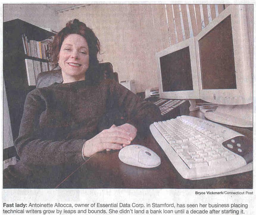 A picture of Antoinette Allocca sitting and smiling in her home office along side her computers and bookshelf