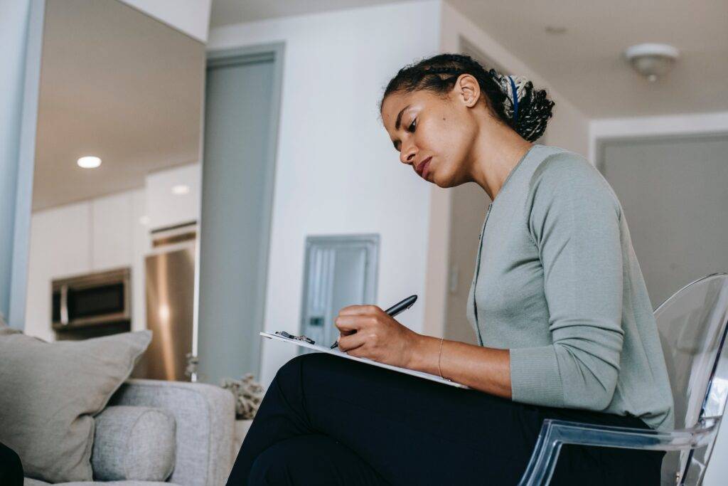 a woman, sitting on a couch, filling out a form, representing the importance of the clear communication Employee Benefits Guide Writing Services provide