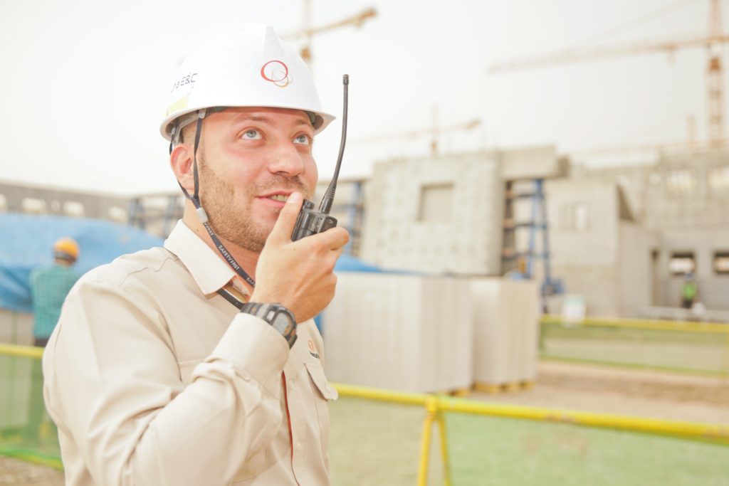 A man wearing a hardhat helmet speaking into a walkie talkie 