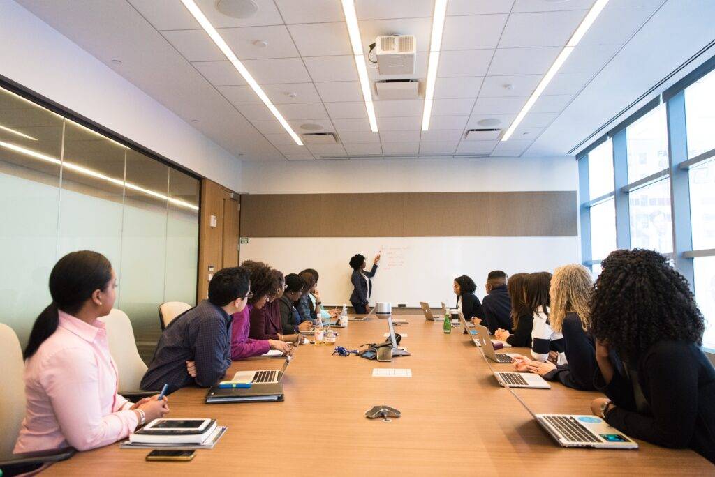 A meeting room with people turned towards a white board, an aid to enhance the definition of training materials.