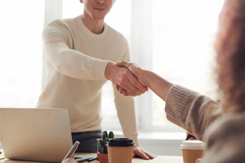 two people shaking hands while reaching over a desk, representing the benefits of an acceptable use policy for employers