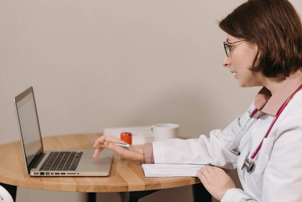 Female doctor writing on a laptop at a table, representing the importance of Medical Writing