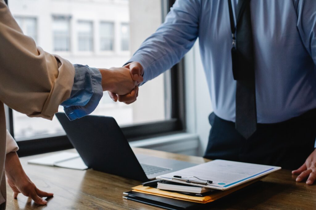 Two people shaking hands over a desk, and it is implied they are about to have a meeting, likely about the benefits of working with cybersecurity technical writers.