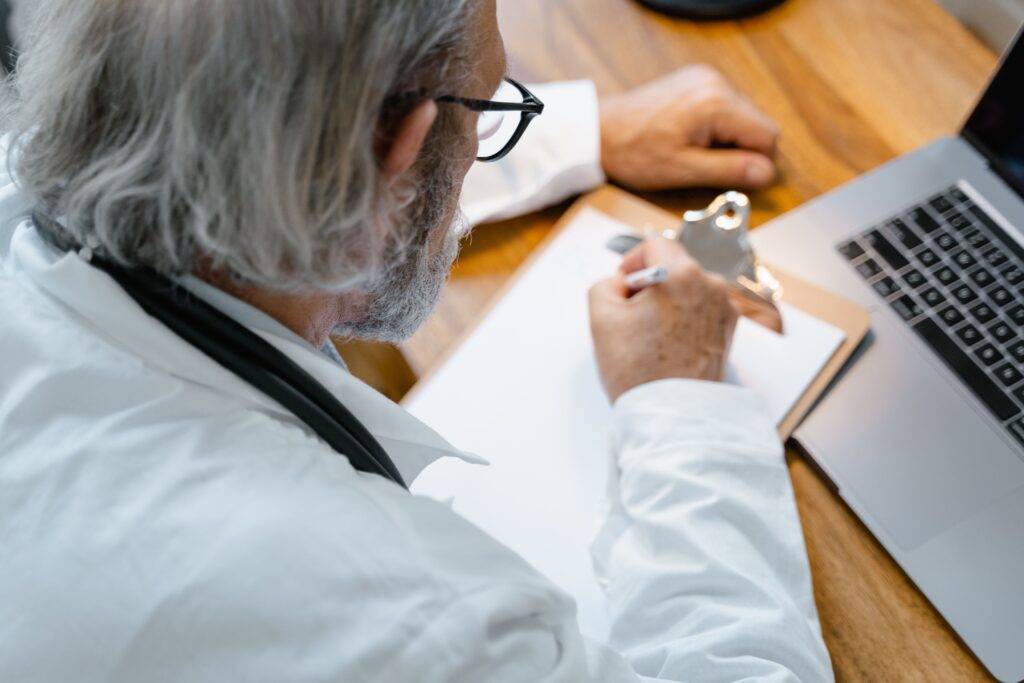 Male Medical Writer wearing a lab coat and writing at a desk, showing an example of What Medical Writing is