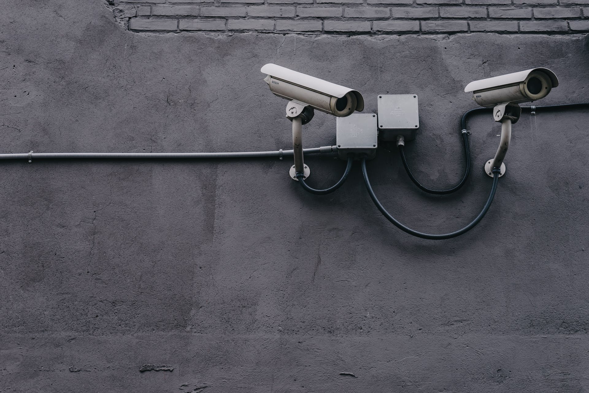 two surveillance cameras on a grey wall, representing the importance of Surveillance User Guides
