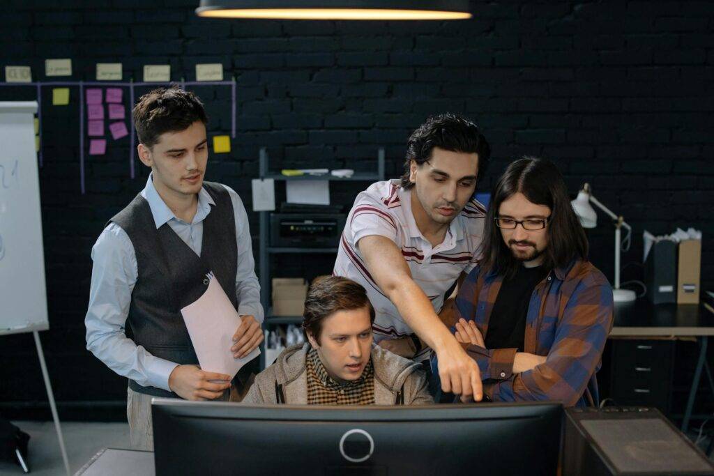 a Group of Employees Discussing a Project While Looking at a Computer, Representing the Importance of Communication in Employee Training Manuals