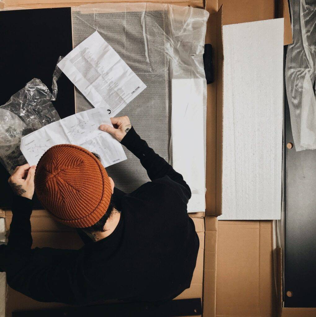 a young adult in a red beanie reading a user manual while assembling furniture, representing the importance of user manual writing services