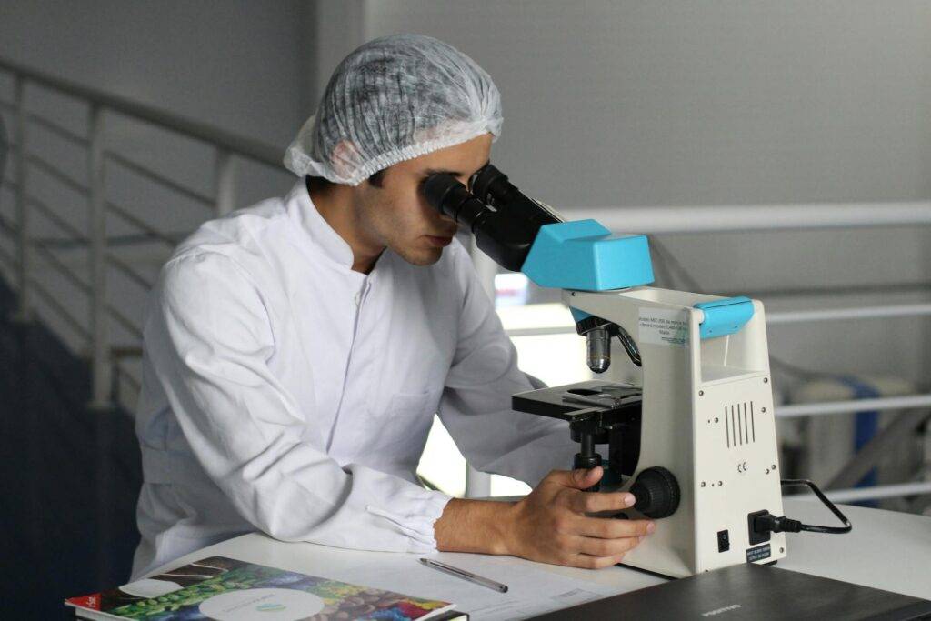 a Medical Researcher Looking through a Microscope, gathering Data that a Medical Writer will Document and Communicate