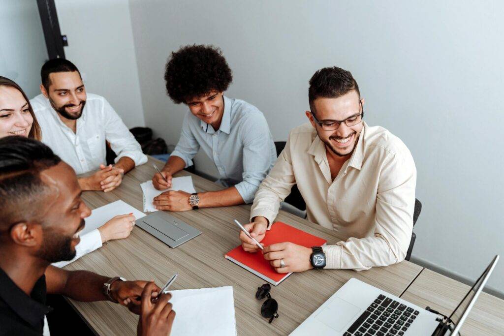 a Group of Smiling Employees Sitting around a Conference Table, Representing the Benefits to Understanding Why Are Technical Writers Important